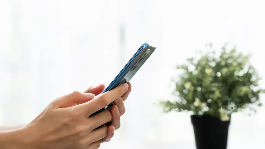 Person holding smartphone near window and plant ready to contact Pomona attorney for workers compensation medical benefits assistance in California